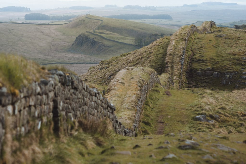 A wide section of Hadrian's Wall curving over the hills in the distance