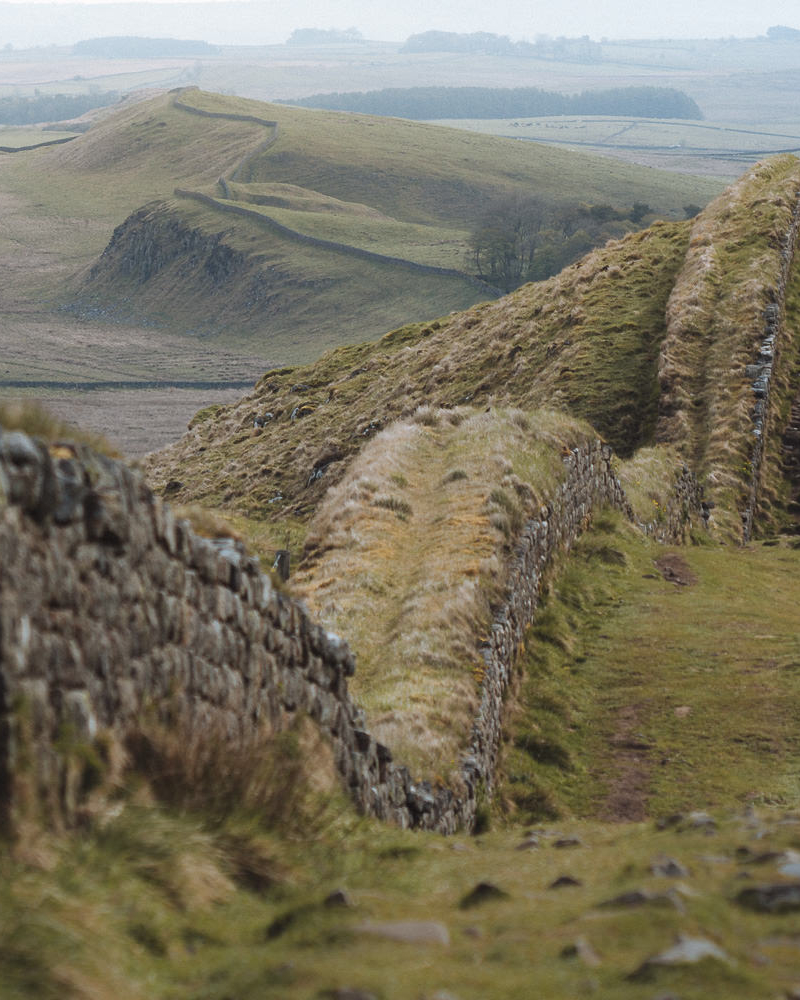 A wide section of Hadrian's Wall curving over the hills in the distance