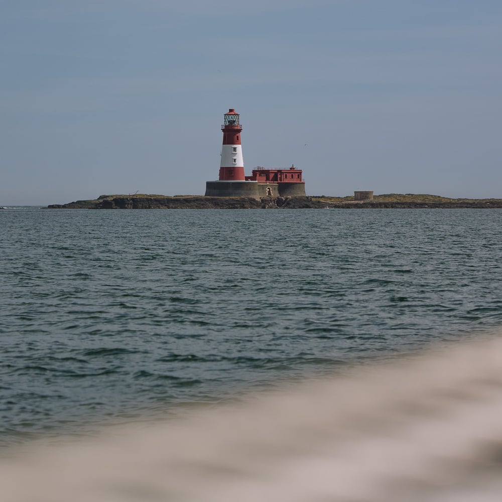 red and white lighthouse on the horizon with sea in the foreground