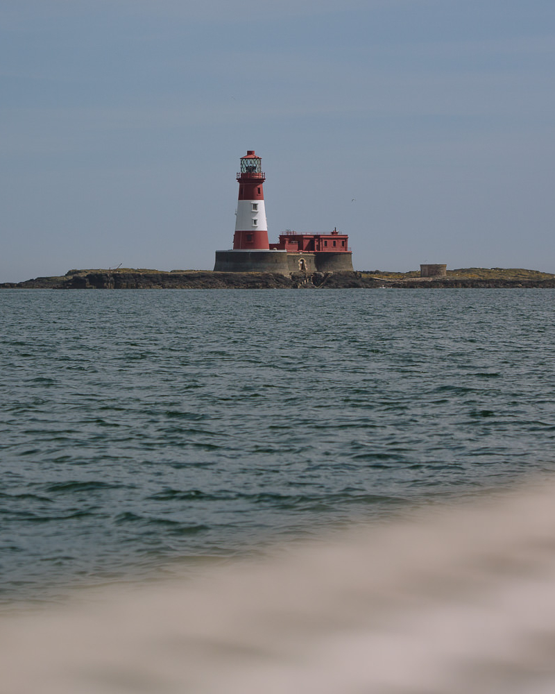 red and white lighthouse on the horizon with sea in the foreground