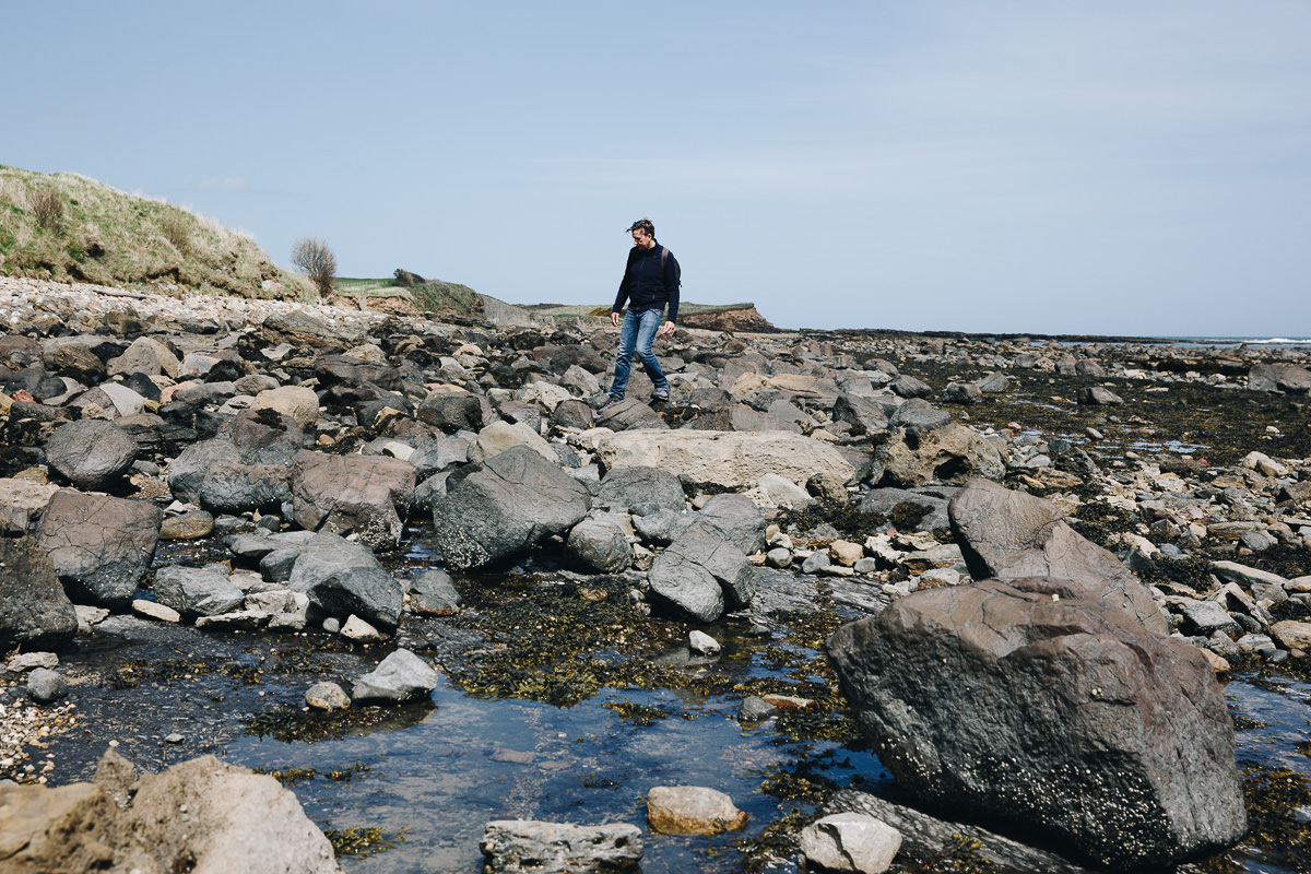 man walks over rocks in a tidal section of the coast