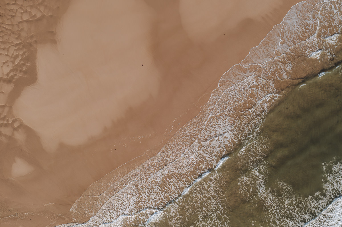 aerial top down shot of a large sandy beach with gentle waves breaking