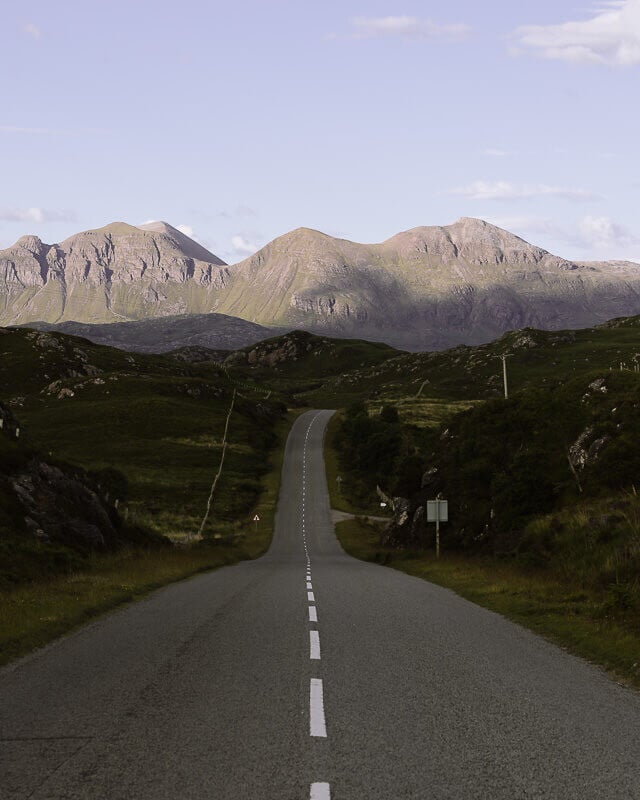 road leads through crinkly hills to a mountain backdrop in Assynt, Scotland