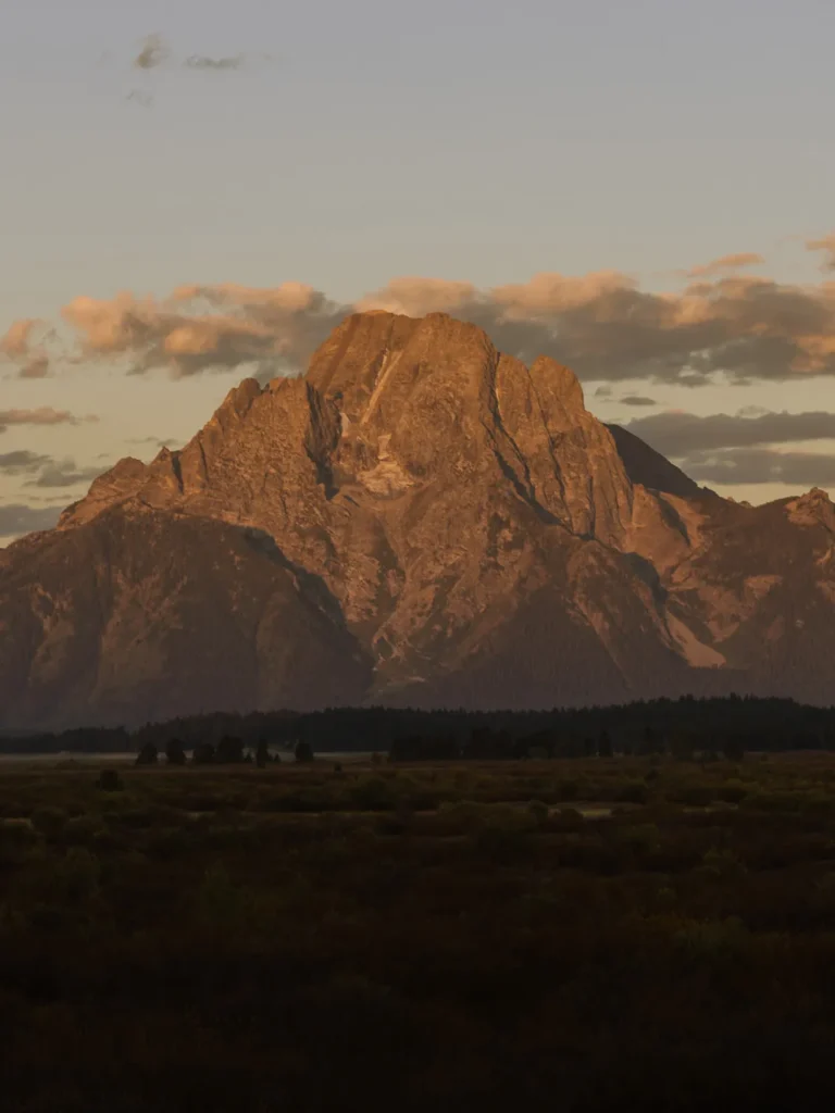 Grand Teton peaks glowing in golden light above the valley at sunrise.