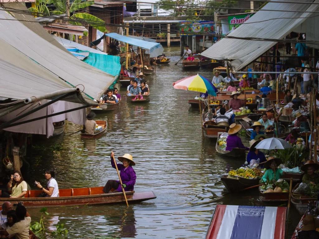 Boats carrying vendors and tourists navigate the busy canals of Damnoen Saduak floating market, Thailand.