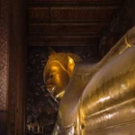 The giant gilded Reclining Buddha statue inside Wat Pho temple, Bangkok, with ornate painted walls visible in the background.