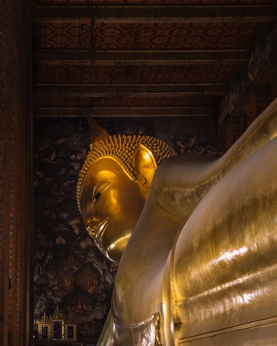 The giant gilded Reclining Buddha statue inside Wat Pho temple, Bangkok, with ornate painted walls visible in the background.
