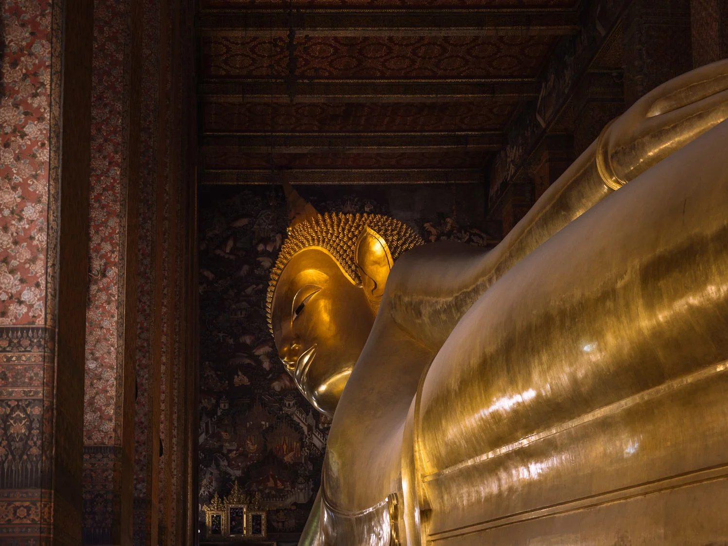The giant gilded Reclining Buddha statue inside Wat Pho temple, Bangkok, with ornate painted walls visible in the background.