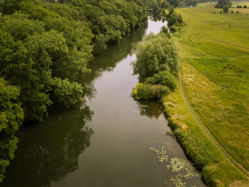 Aerial view of the River Thames at Clifton Hampden, with lush green meadows and dense woodland lining the calm, tree-lined water