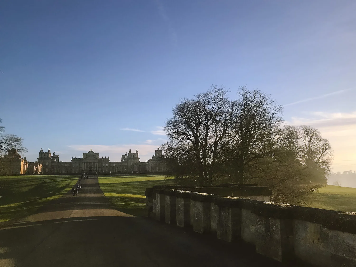 Blenheim Palace viewed across its landscaped parkland in Oxfordshire, with a stone bridge and low evening light.