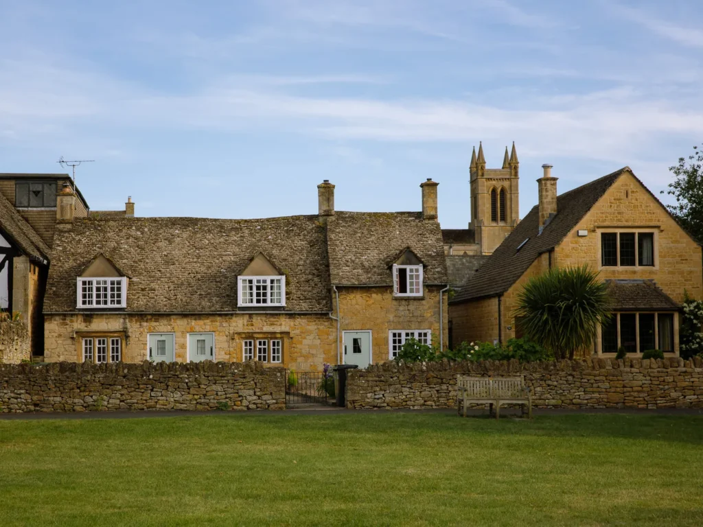 Honey-coloured stone cottages and church tower overlooking a village green in Broadway, Cotswolds.