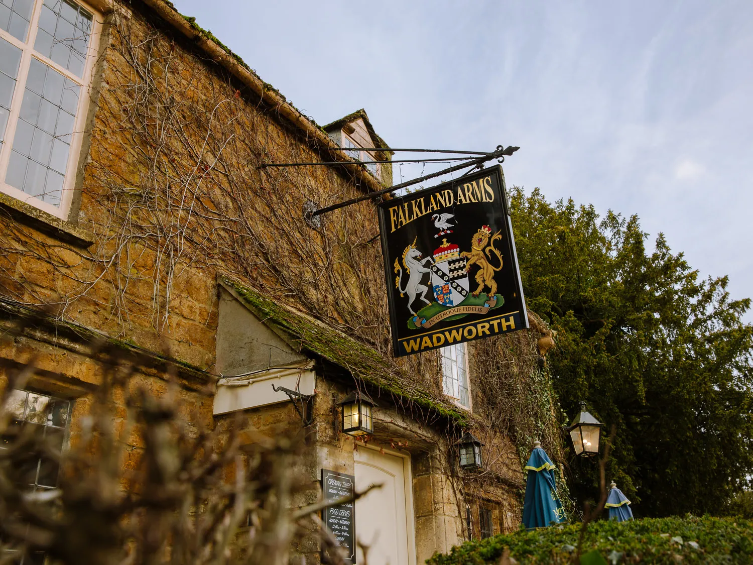 Traditional Falkland Arms pub sign hanging outside a honey-coloured stone building in Great Tew, Cotswolds.
