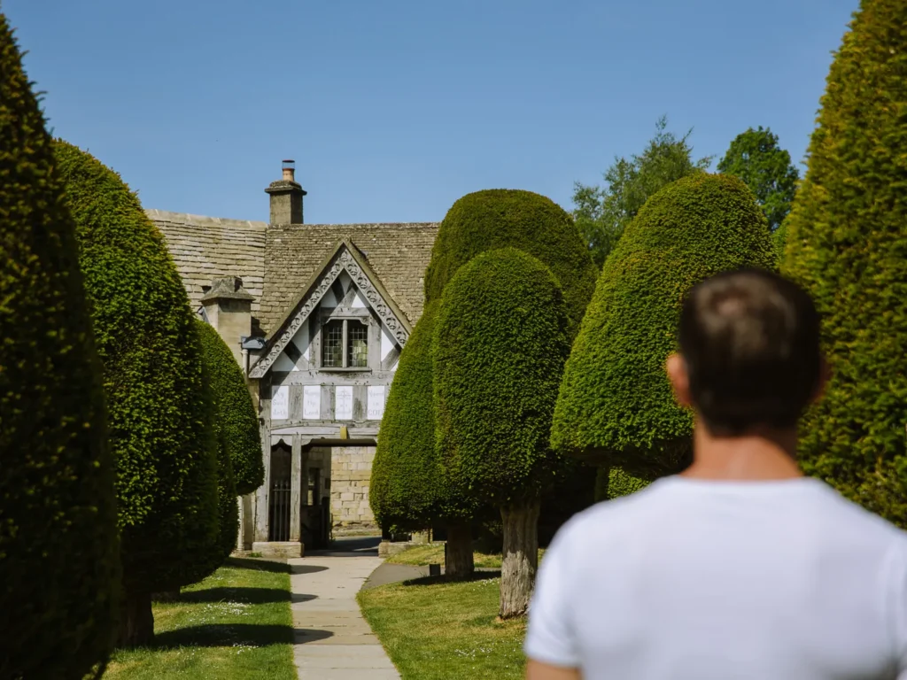 Sculpted yew trees lining the path through St Mary’s churchyard in Painswick, with historic stone buildings beyond.