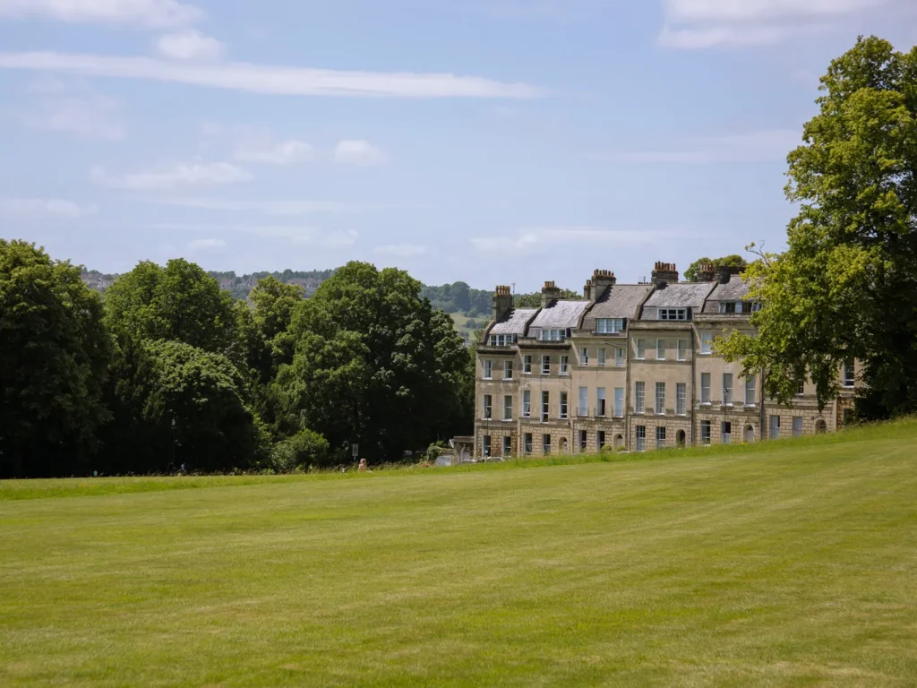 Georgian townhouses overlooking a wide green lawn surrounded by mature trees in Bath, England.