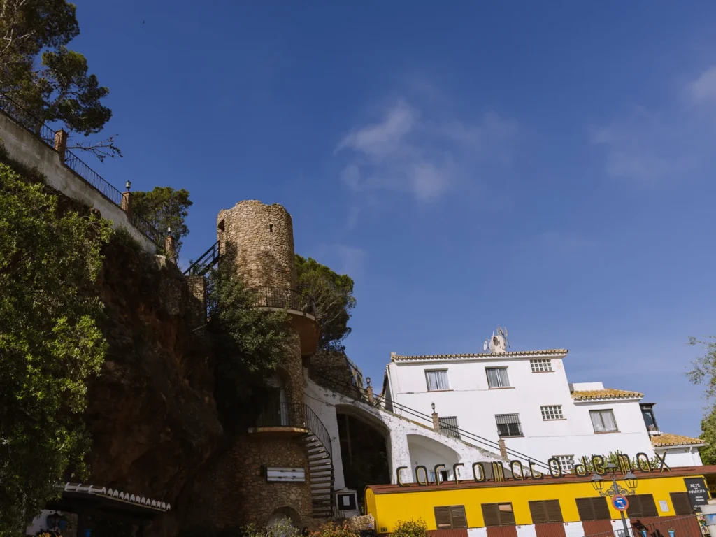 The Flour Mill and Miniature Museum in Mijas Pueblo, with the old castle tower and rocky cliff above and the distinctive yellow Miniature Museum building below
