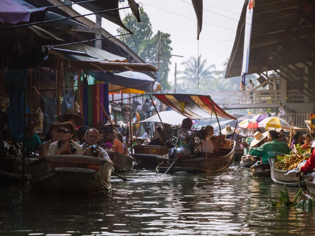 Tourists in boats navigate colorful market stalls along canal at Damnoen Saduak Floating Market