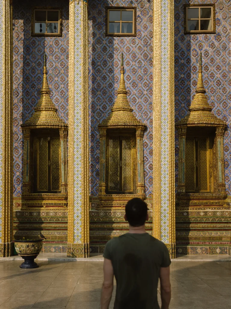 Golden spires on blue mosaic walls at Wat Phra Kaew, Grand Palace Bangkok with visitor.