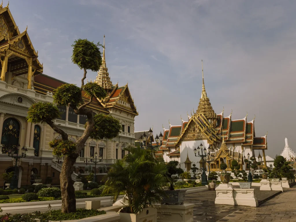 Ornate golden pavilions with red roofs and bonsai trees at Bangkok Grand Palace.