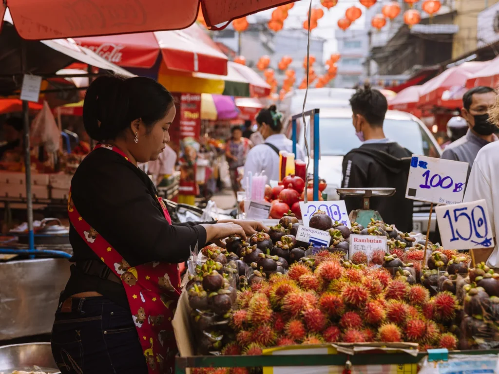 Woman sells rambutan and mangosteen at bustling Bangkok Chinatown market stall amid red lanterns