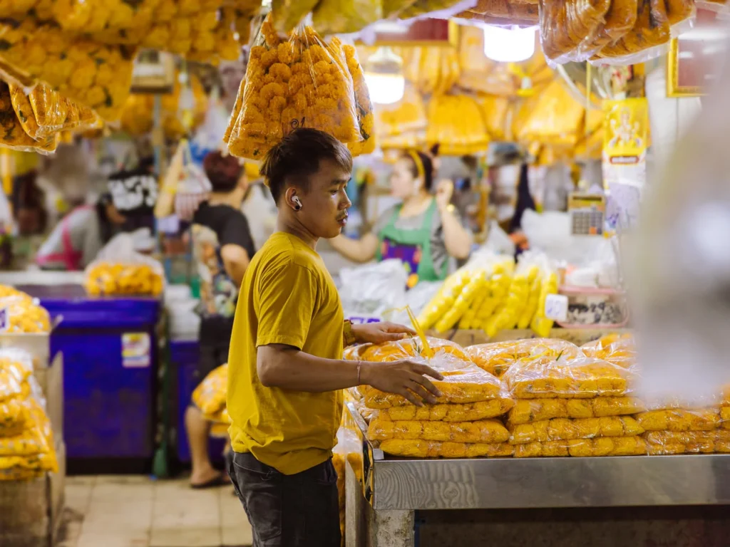 Young vendor handling bags of marigolds at Pak Khlong Talat wholesale flower market, Bangkok