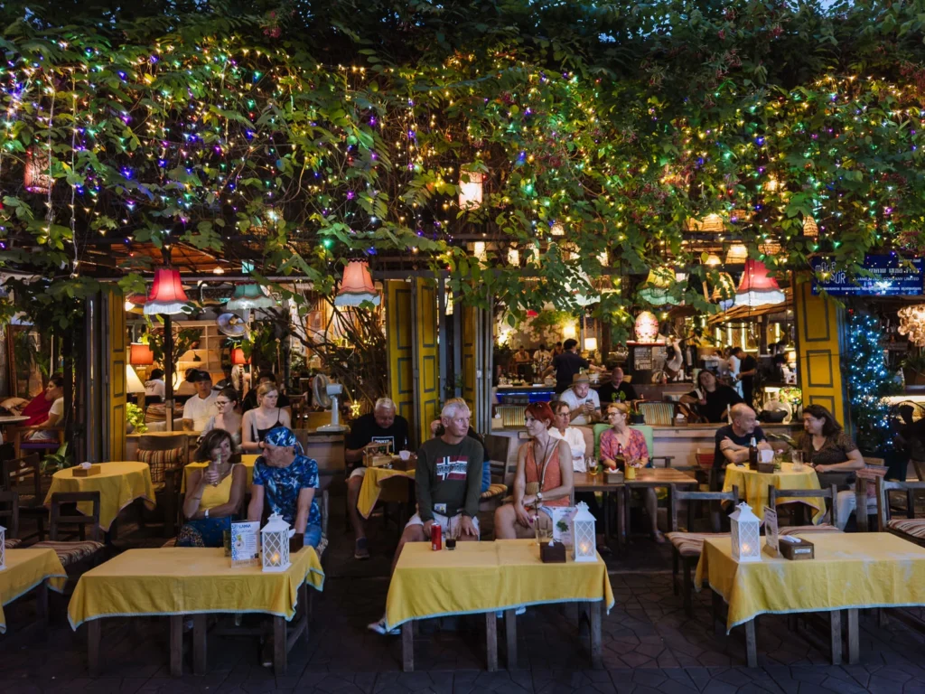 Tourists dine under string lights and lanterns at vibrant Khao San Road restaurant in Bangkok at night.