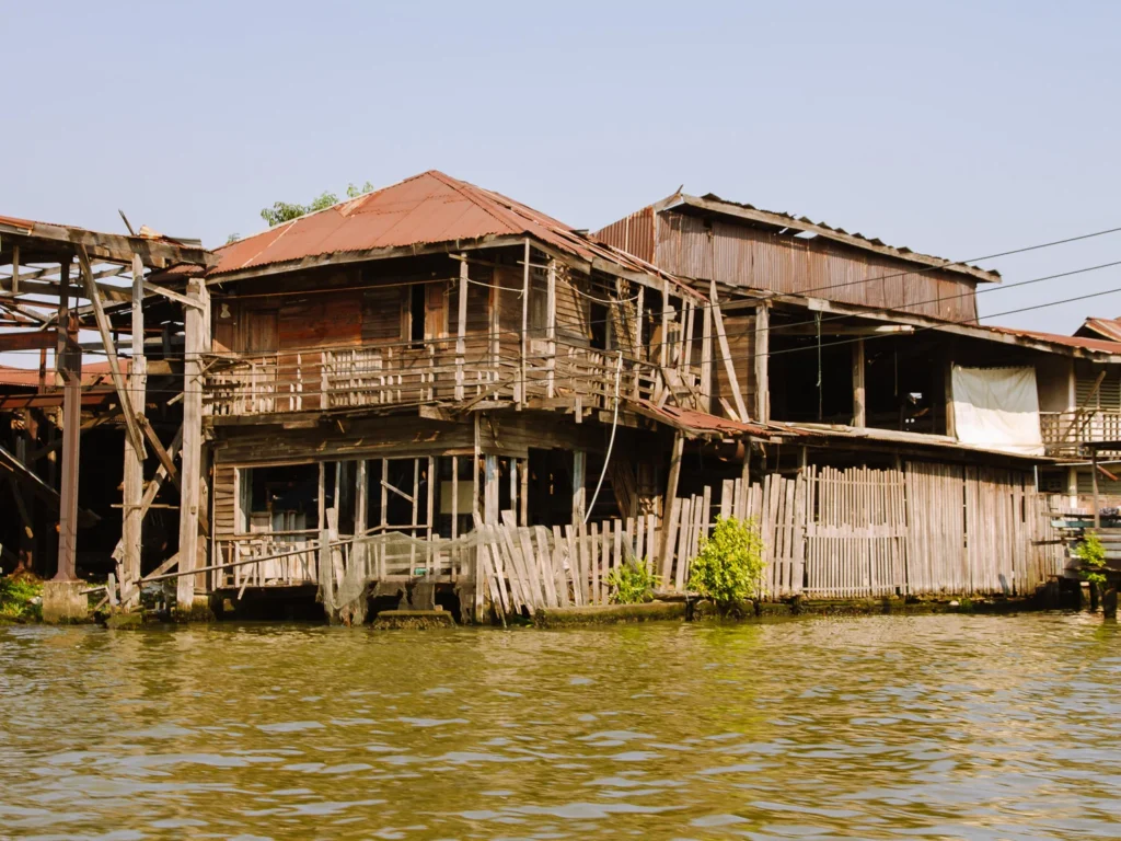 Rustic wooden stilt houses on stilts over Bangkok klong, with weathered roofs and river views.