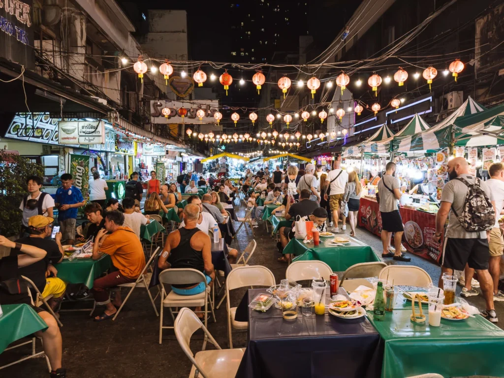 Bustling nighttime street food market in Silom, Bangkok, with crowds dining under red lanterns.
