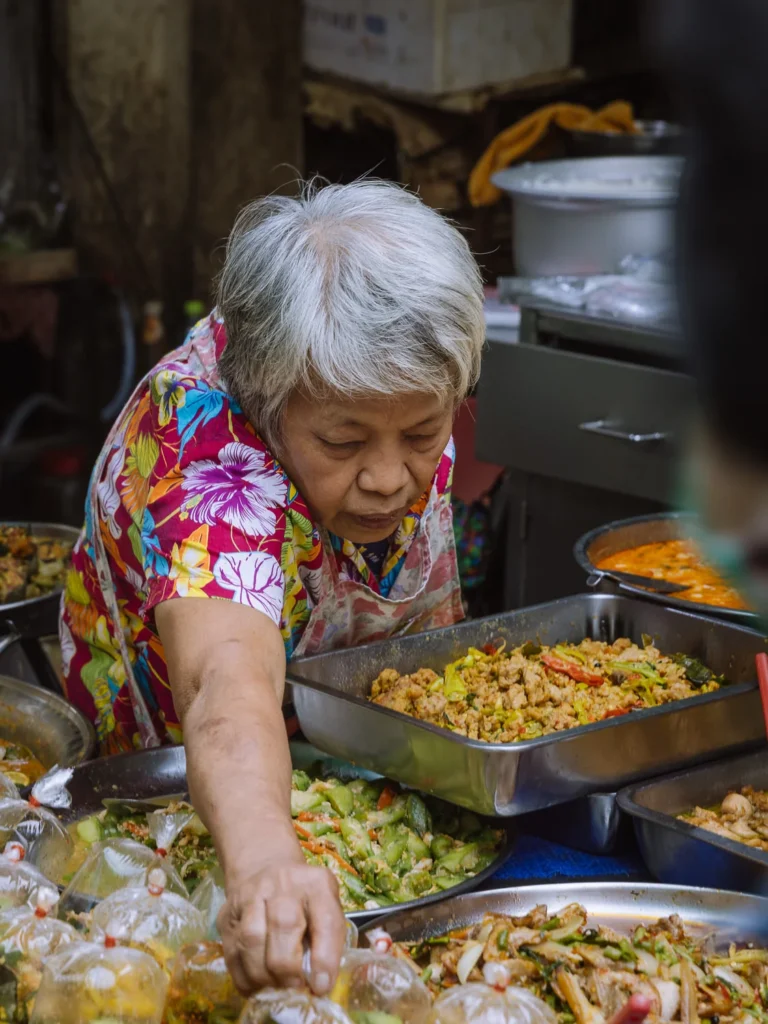 Food vendor serving fried chicken and stir-fried dishes at Trok Mor morning market, Bangkok