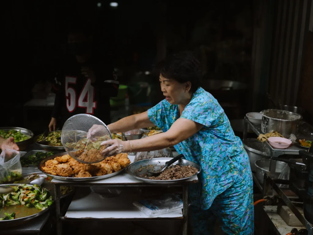 Food vendor serving fried chicken and stir-fried dishes at Trok Mor morning market, Bangkok