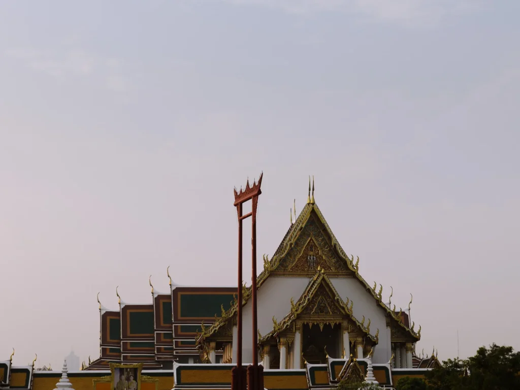 Wat Suthat temple's golden gabled hall with red trim before giant swing in Bangkok at dusk.