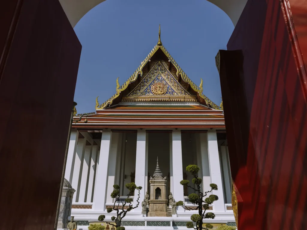 Framed view through red doors of Wat Suthat's ornate golden-roofed hall and stupa in Bangkok.