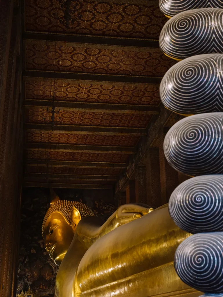Reclining golden Buddha statue with black spiral finials under ornate ceiling at Wat Pho Bangkok.