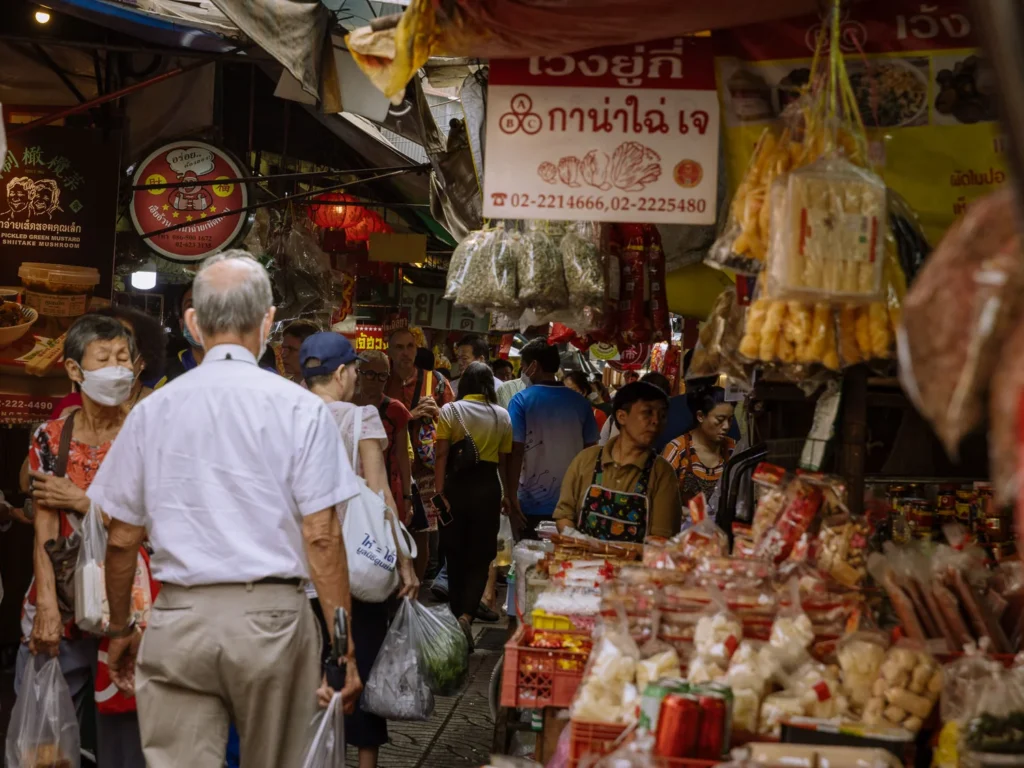 Shoppers browse a narrow, crowded lane in Bangkok's Chinatown, lined with stalls selling dried goods and packaged foods.