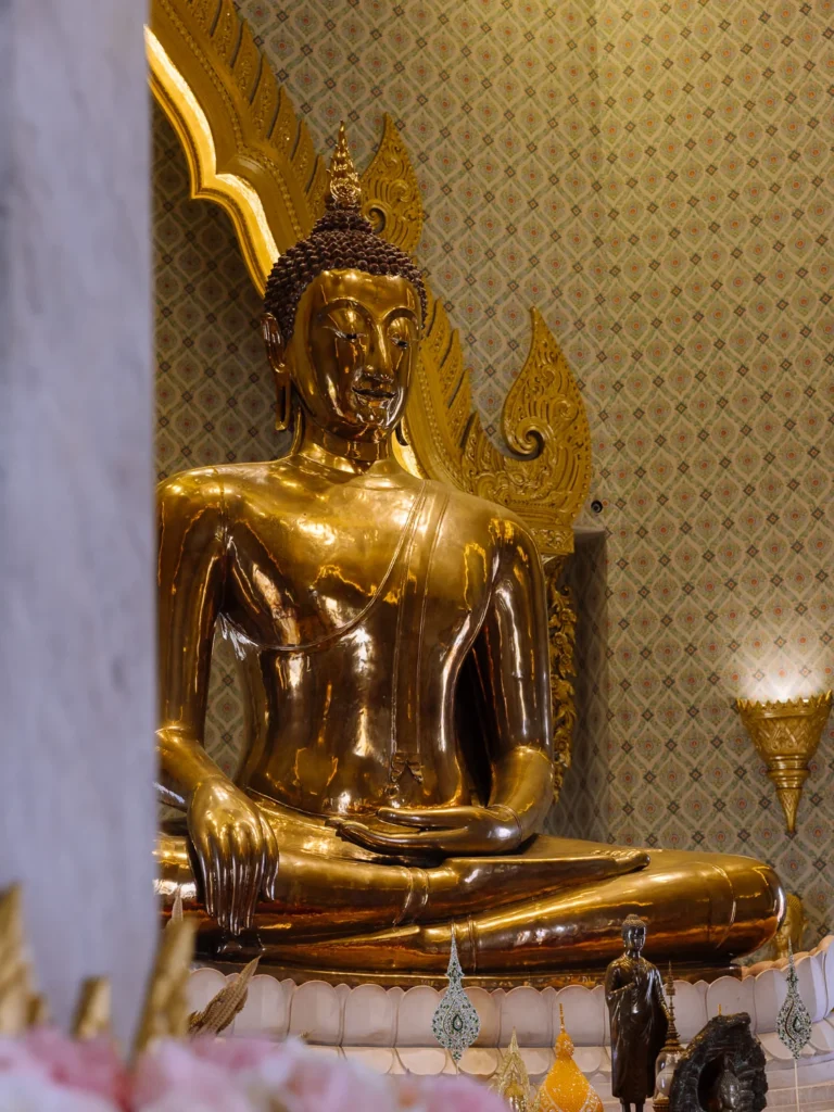 The solid gold Buddha statue at Wat Traimit, Bangkok, gleaming under soft light with a golden flame halo behind it.