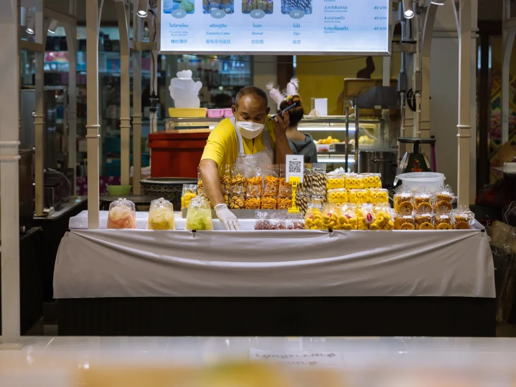 Vendor arranging Thai snacks and sweets at a market stall in Bangkok