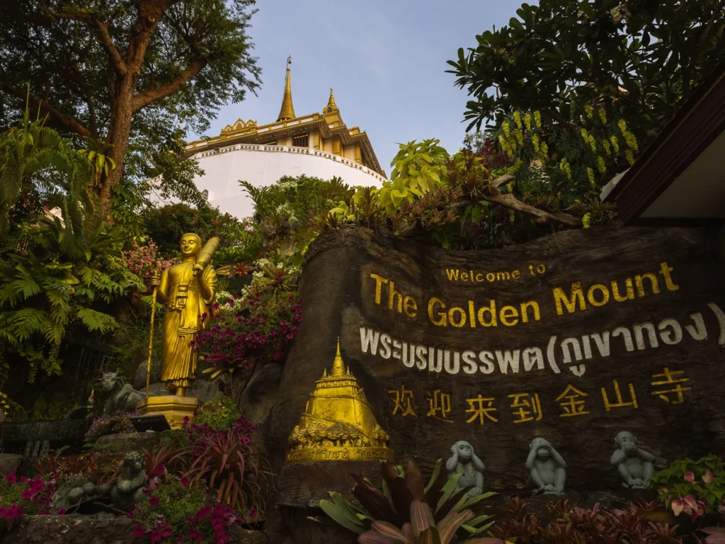 Welcome sign and golden Buddha statue at the entrance to Wat Saket, the Golden Mount temple, Bangkok