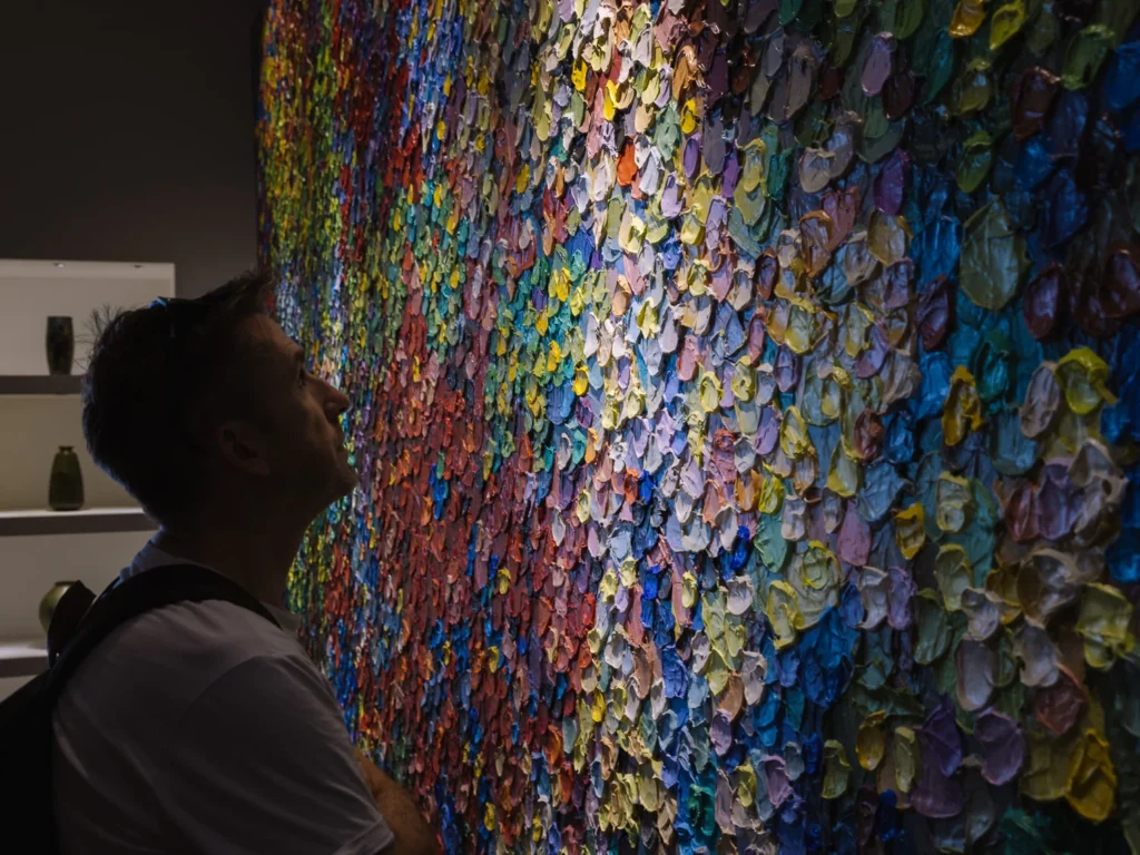 A visitor looks up at a large textured painting covered in densely layered multicoloured brushstrokes at ATT 19, Bangkok.