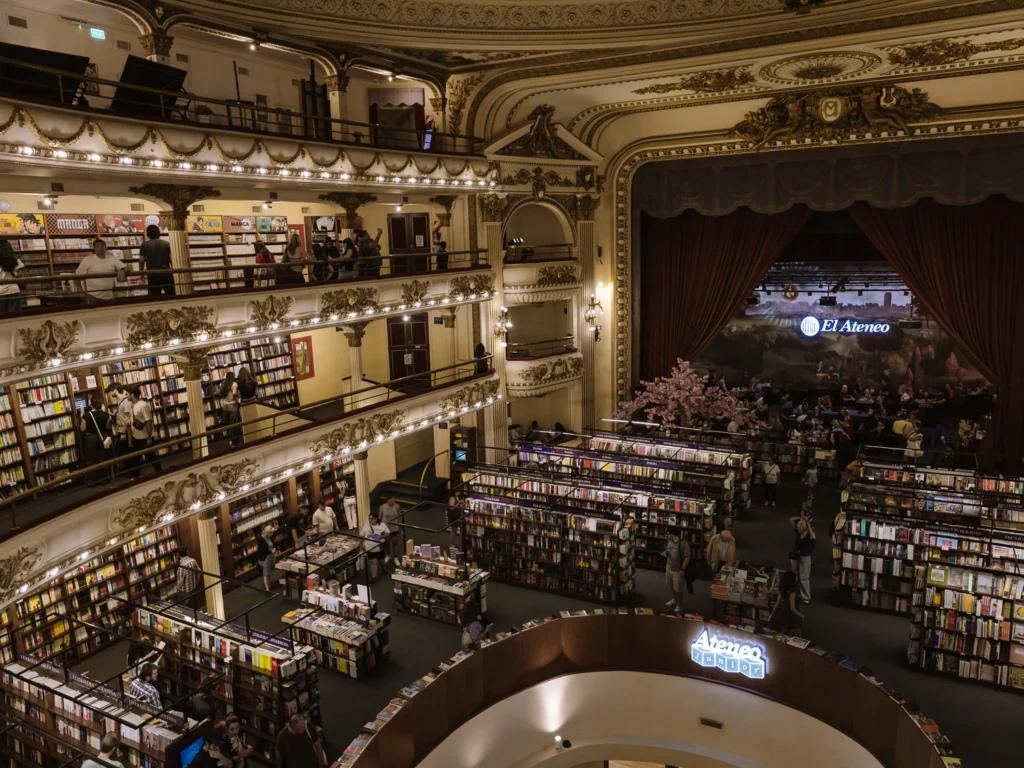 The interior of El Ateneo Grand Splendid bookshop in Buenos Aires, showing rows of books filling the stalls floor, gilded balconies lined with bookshelves, and the original stage now used as a café