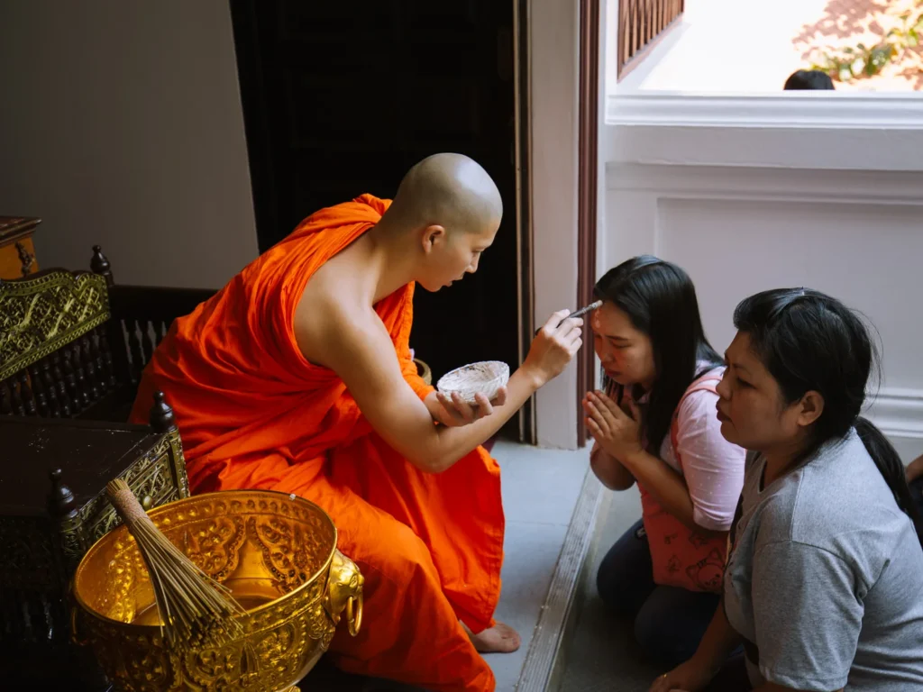 A Buddhist monk applies a blessing mark to the forehead of a kneeling woman at Wat Saket, Bangkok.