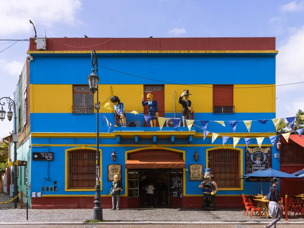 A brightly painted blue and yellow building on Caminito street in La Boca, Buenos Aires, with life-size figurines of Diego Maradona, Eva Perón and a tango dancer on the balcony