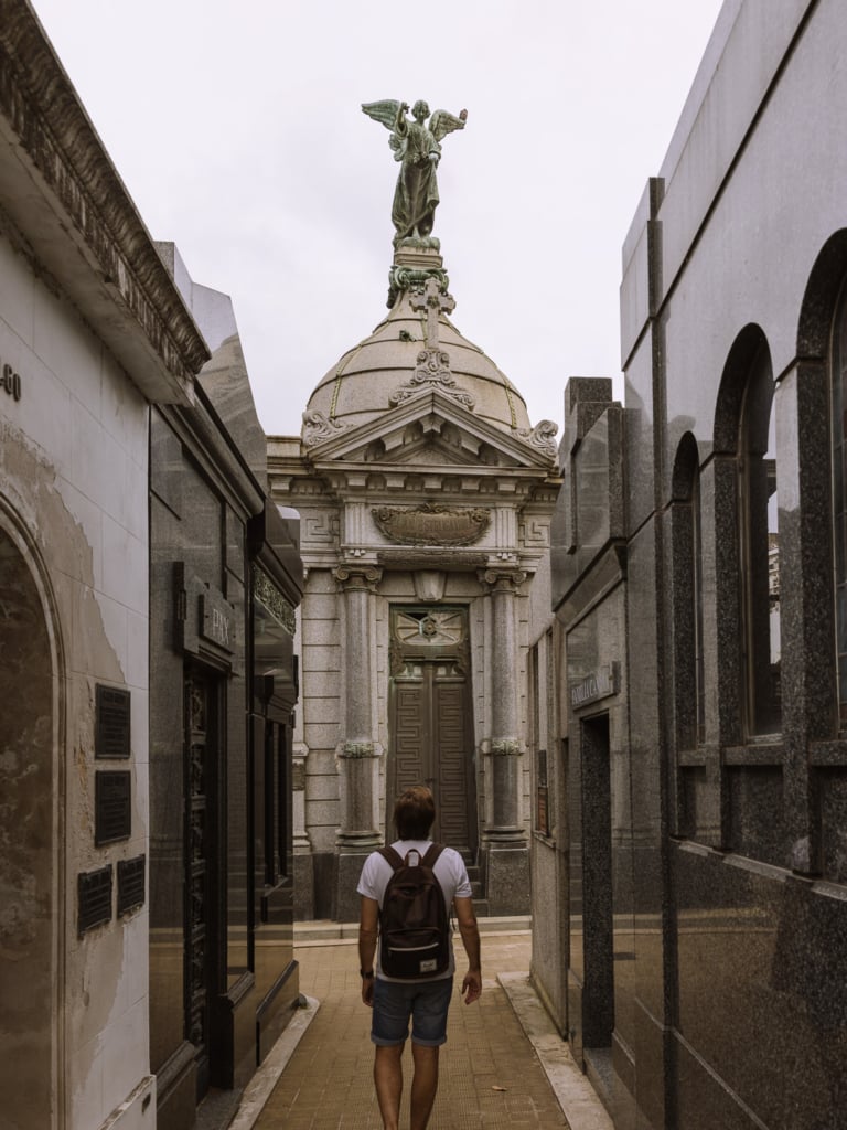 Mark looking up at an ornate domed mausoleum topped with a bronze angel statue in Recoleta Cemetery, Buenos Aires