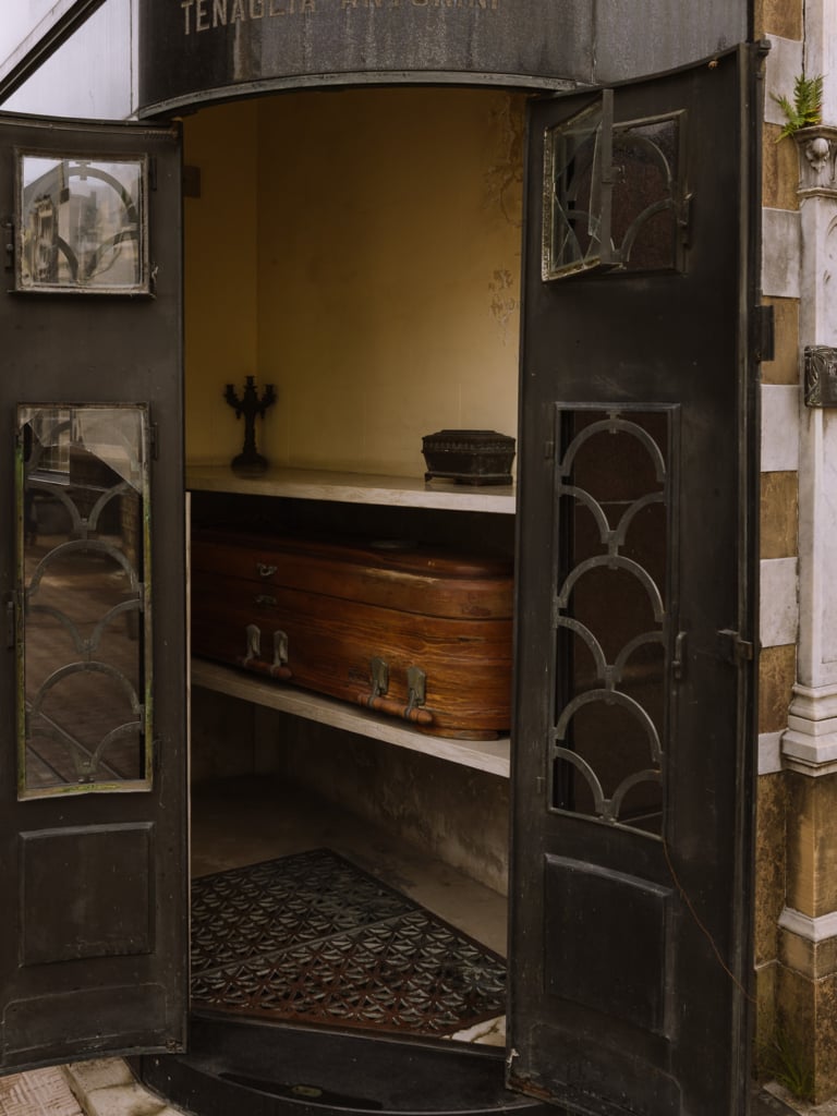 The open door of a mausoleum at Recoleta Cemetery in Buenos Aires, with a wooden coffin on display inside alongside a candelabra