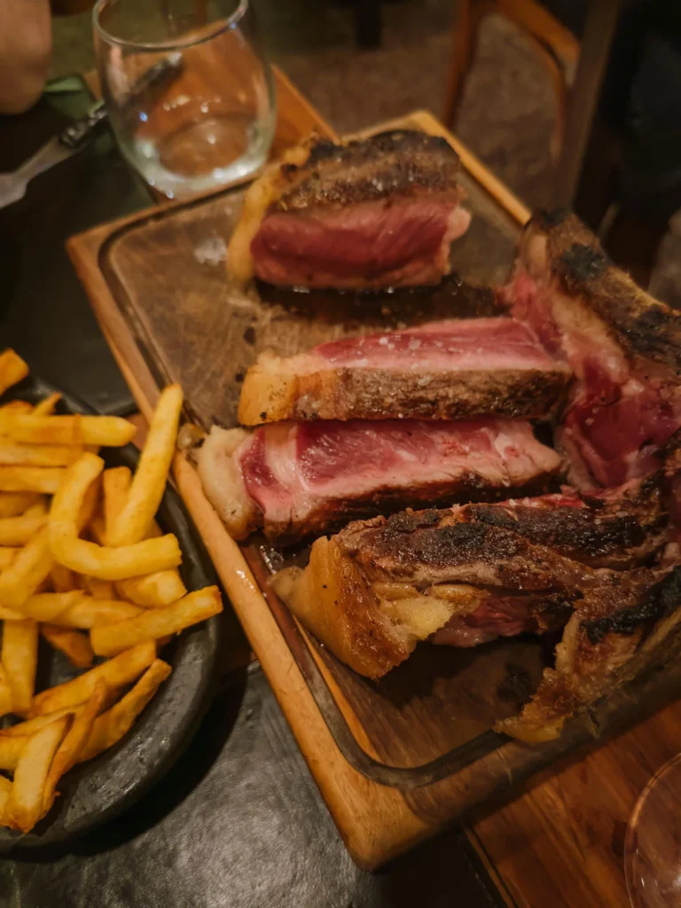 Sliced Argentine ojo de bife (ribeye steak) on a wooden board at a Buenos Aires parrilla, showing a pink, medium-rare interior with a charred crust, served with a side of crispy chips