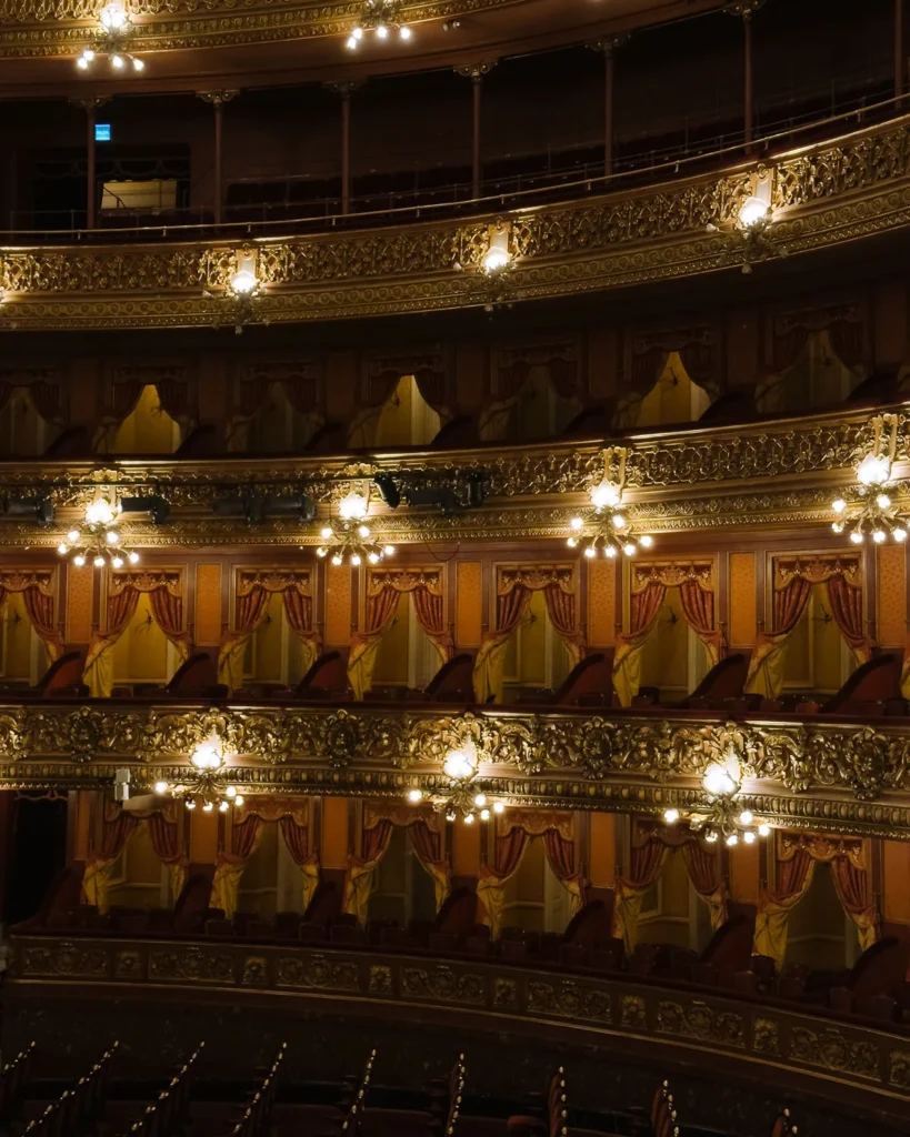 The ornate gilded balconies and curtained private boxes inside the Teatro Colón opera house in Buenos Aires, illuminated by warm chandelier light
