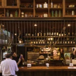 The rustic interior of a Buenos Aires parrilla, with hanging sausages, cuts of meat on display, wine bottles lining the shelves, and diners seated at a wooden bar counter