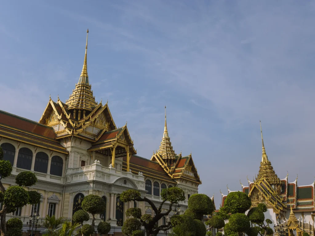 The Chakri Maha Prasat throne hall at the Grand Palace, Bangkok, its European neoclassical facade topped with ornate Thai spires against a blue sky.