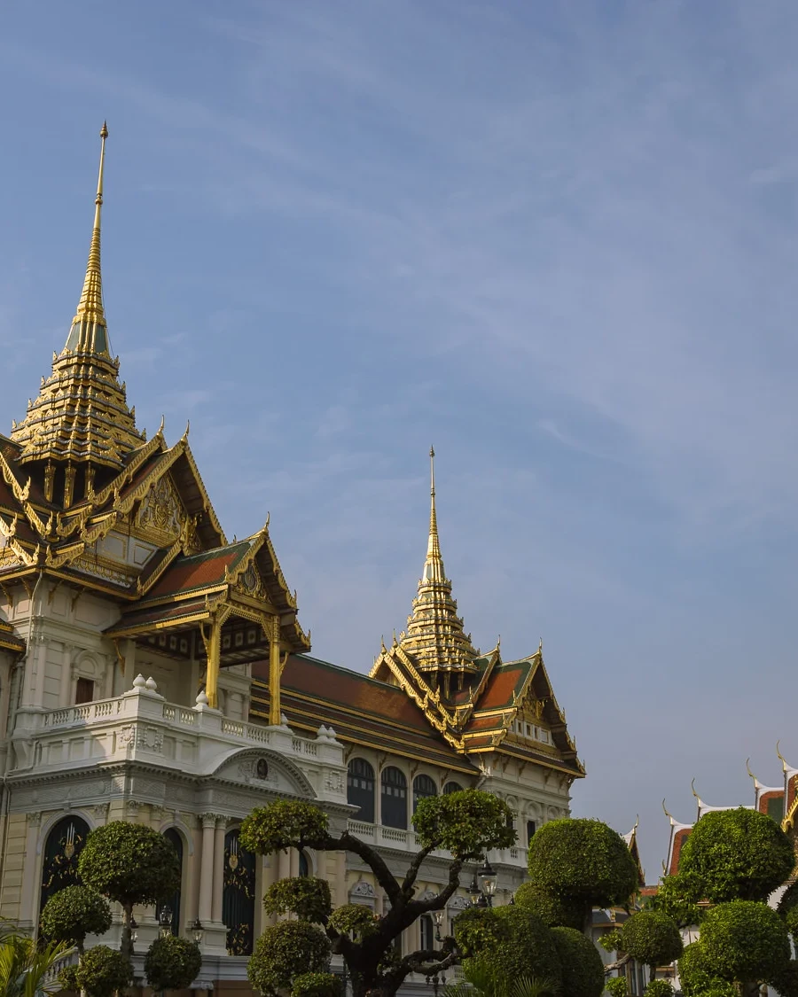 The Chakri Maha Prasat throne hall at the Grand Palace, Bangkok, its European neoclassical facade topped with ornate Thai spires against a blue sky.