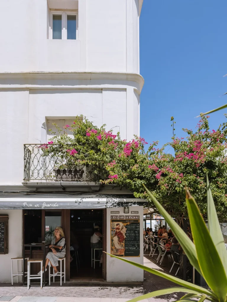 The exterior of Bar El Francés in Tarifa, a white building draped in pink bougainvillea with outdoor terrace seating and a woman sitting at the entrance on a sunny day