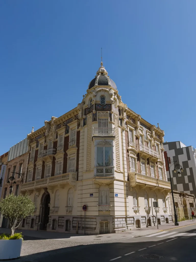 The Palacio de Aguirre in Cartagena, Spain — an ornate Modernista building designed by Víctor Beltrí, featuring a corner tower with a tiled dome, decorative balconies, and richly detailed facades