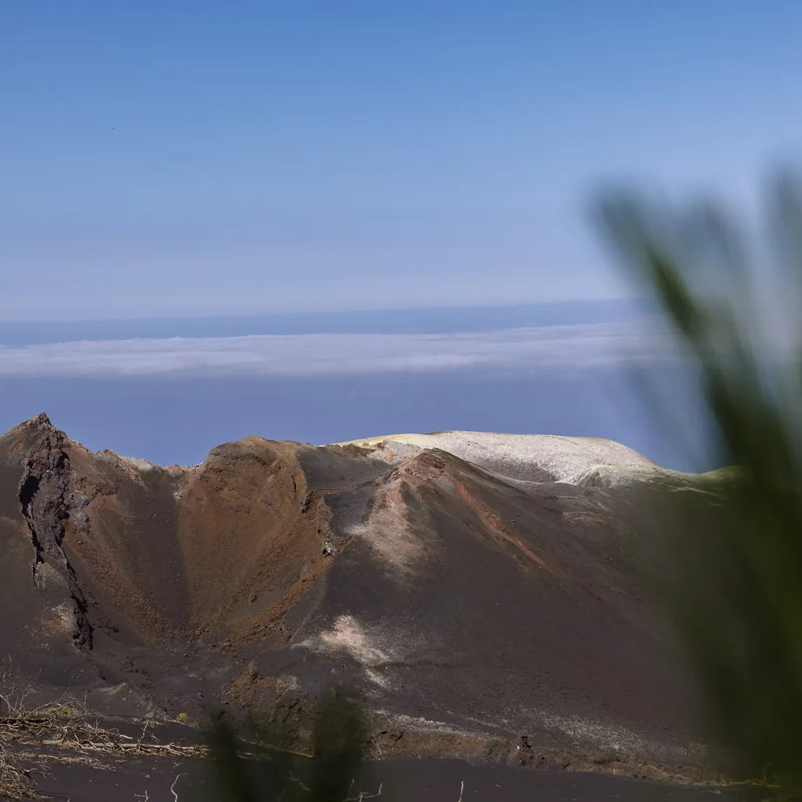 Volcanic crater landscape on La Palma in the Canary Islands, with rugged dark slopes, a pale ridge, and ocean clouds in the distance.